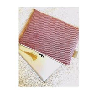 Peut inclure: Une pochette zippée en velours côtelé rose avec un pompon doré. La pochette est ouverte et une tablette blanche est à l'intérieur.