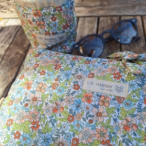 Può includere: Una pochette in tessuto bianco con un motivo floreale e un cordoncino in pelle marrone. La pochette ha un'etichetta che dice "LN Atelier Fait Main".