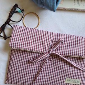 Op de afbeelding: Een rechthoekig stoffen tasje met een rood-wit ruitpatroon, voorzien van een omslagflap die wordt vastgezet met twee stoffen linten. Een rechthoekig label met de tekst LN Atelier is op de rechterbenedenhoek genaaid.