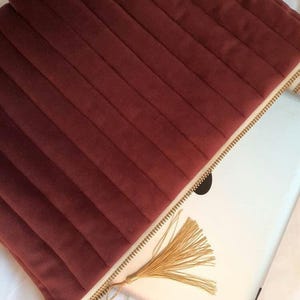 Puede incluir: Una funda para portátil de terciopelo burdeos con cremallera dorada y borla. La funda está forrada con un tejido crema.