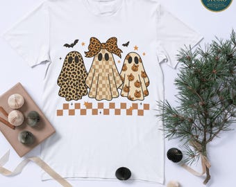 May include: White t-shirt featuring three ghost characters with different patterns: leopard print, checkered, and pumpkin-themed. The ghosts have black eyes and are decorated with bats and stars. The shirt has the text "PNG File - Digital Download Only (No Physical Item)".