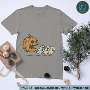 Puede incluir: Una camiseta gris con un diseño de Halloween. El diseño presenta una calabaza naranja con una expresión amenazante, persiguiendo a tres fantasmas blancos. El texto en la parte inferior dice "PNG File - Digital Download Only (No Physical Item)".