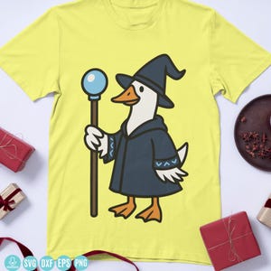 May include: A yellow t-shirt with a cartoon illustration of a goose in a wizard's outfit. The goose is depicted with a blue hat and robe, holding a staff with a blue orb. A fun and quirky design.