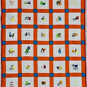 May include: An alphabet quilt with embroidered letters and animal images. The quilt has a grid design with orange, blue, and white squares. The text "Now I know my" and "Will you come" are embroidered on the quilt.