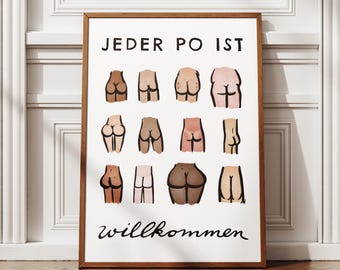 May include: A framed art print featuring illustrations of various buttocks in different skin tones. The text "Jeder Po ist willkommen" is displayed in black script at the bottom of the print. The artwork is displayed on a wooden floor.