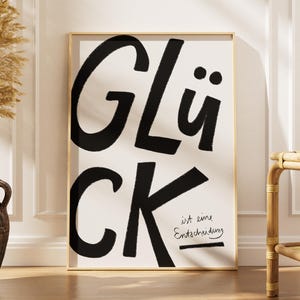 Könnte beinhalten: Ein gerahmter Kunstdruck mit dem Wort "GLÜCK" in großen, fetten, schwarzen Buchstaben, darunter "CK". Darunter steht der Satz "ist eine Entscheidung" in einer kleineren, handschriftlichen Schrift. Der Druck befindet sich in einem goldenen Rahmen.
