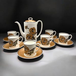 May include: A vintage tea set featuring a white coffee pot and matching cups and saucers. The set is decorated with brown floral designs and a gold rim. The set includes a coffee pot, six cups, and six saucers.