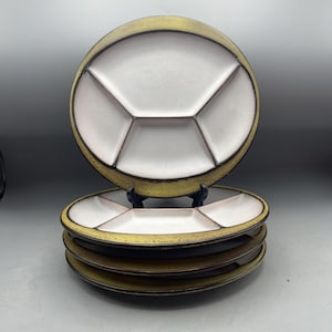May include: A stack of six ceramic serving plates. Each plate has a white interior divided into four sections, with a brown border and a gold-colored rim. The plates are stacked on top of each other.