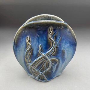 May include: A blue and brown ceramic vase with a wavy design. The vase is shaped like a shell and has a small opening at the top.