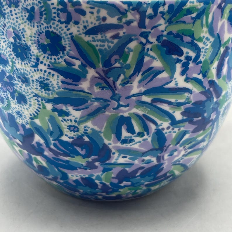 Puede incluir: Un cuenco de cer&aacute;mica con un estampado floral en tonos azules, verdes y morados. El dise&ntilde;o presenta flores y hojas estilizadas sobre un fondo blanco. La superficie del cuenco es lisa y brillante, con forma redondeada.