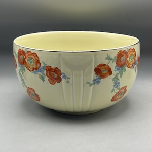以下が含まれることがあります： クリーム色のセラミックボウル、花柄のデザイン。 ボウルは、暗いトリムとオレンジと青の花のパターンを備えたリムが特徴です。 ボウルには側面に垂直の溝があります。