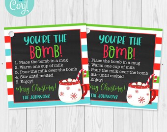 May include: Two rectangular cards with a black chalkboard background and colorful borders. The text "YOU'RE THE BOMB!" is at the top, with instructions below. A mug graphic with marshmallows and a candy cane is also featured. The words "Merry Christmas!" and a name are at the bottom.