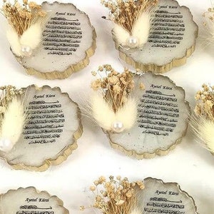 May include: A set of 10 wooden ornaments with a white feather and dried flowers. Each ornament features a decorative design with the text "Ayetel K&uuml;rsi" in Arabic script.
