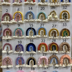 May include: A display of 36 colorful rainbow keychains with gold key rings. Each keychain is made of yarn and has a different color combination. The keychains are arranged in rows of six, with numbers 1 through 36 labeling each keychain.