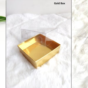 May include: A white circular plaque with gold trim and Arabic calligraphy. The plaque is on a clear acrylic stand. The plaque is also shown in a gold box with a clear lid and a brown cardboard box with a clear lid.