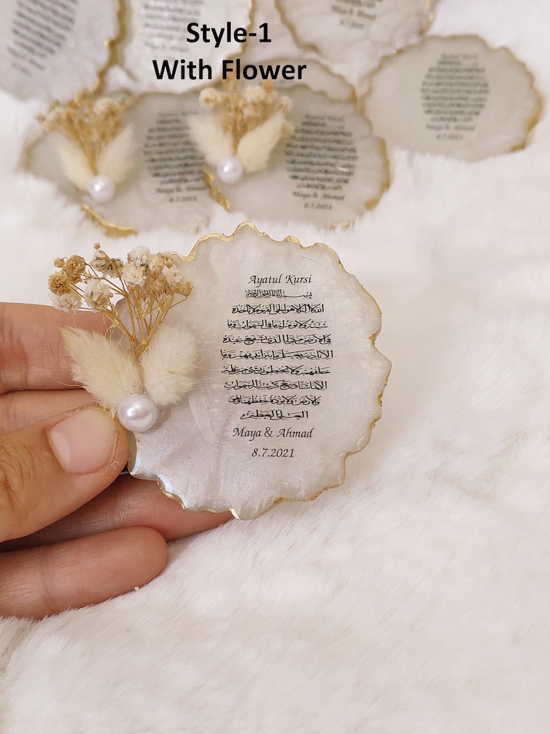 May include: White resin coaster with a gold rim and a printed Islamic prayer in Arabic script. The coaster is decorated with dried flowers and a pearl. The text on the coaster reads "Ayatul Kursi" and includes the date "8.7.2021".