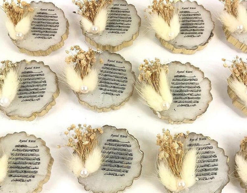 May include: A set of 10 wooden ornaments with a white feather and dried flowers. Each ornament features a decorative design with the text "Ayetel K&uuml;rsi" in Arabic script.