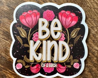 May include: A sticker with a black background and a white scalloped border. The sticker features the words "BE KIND OF A BITCH" in white, outlined in gold. Pink flowers and gold leaves surround the text.