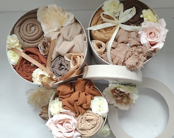 May include: Three round gift boxes filled with brown and beige fabric squares and decorated with pink and white flowers.