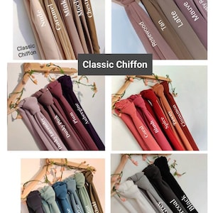 May include: A display of 20 different colors of classic chiffon fabric. The fabric is arranged in rows of 5, with each color labeled with its name. The colors include nude, caramel, mink, mocha, chestnut, rosewood, tan, latte, mauve, dusty lavender, dusty pink, plum, aubergine, white, light grey, charcoal, black, coral, blush, and spice.