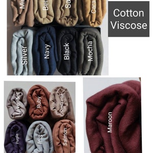 May include: Assortment of rolled fabric swatches in various colors, including purple, lavender, silver, mink, iris, ruby, navy, beige, dusty pink, salmon, black, sand, mocha, caramel, and maroon. The fabric is labeled "Cotton Viscose".