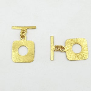 Peut inclure: Deux fermoirs métalliques dorés de forme carrée avec une ouverture circulaire. Les fermoirs sont conçus pour être fixés à des bijoux ou à d'autres articles.