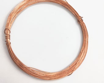 Puede incluir: Alambre de cobre enrollado, de color marrón rojizo, dispuesto en forma circular. El alambre está enrollado firmemente, con una pequeña sección envuelta para asegurar la bobina. El fondo es blanco liso.