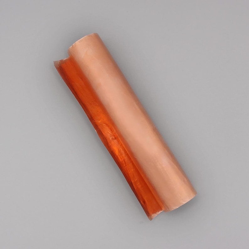 May include: A roll of copper foil with a shiny, metallic finish. The foil is partially unrolled, revealing the orange-brown color underneath.