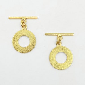 Può includere: Due chiusure a scatto dorate con dischi rotondi testurizzati. Ogni chiusura ha una barra che scorre attraverso il disco.