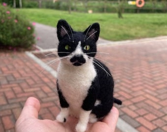 May include: A black and white needle felted cat figurine. The cat is sitting upright with its paws tucked underneath it. It has green eyes and a white patch on its chest.