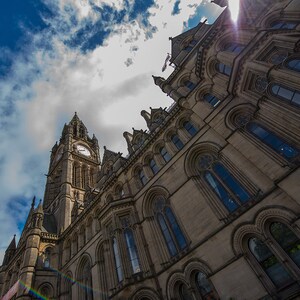 Puede incluir: Una vista de &aacute;ngulo bajo de un gran edificio ornamentado con una torre del reloj. El edificio est&aacute; hecho de piedra y tiene muchas ventanas. El cielo es azul y hay nubes en el cielo.