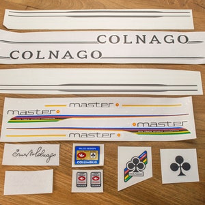 以下が含まれることがあります： 白地に黒文字で「COLNAGO」というブランド名が書かれた、ビンテージな自転車用ステッカーのセットです。ステッカーには、「master」と「COLUMBUS」という文字も黒文字で白地に書かれています。ステッカーは、長方形、楕円形、円形など、さまざまなサイズと形があります。