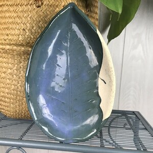May include: A ceramic leaf-shaped dish with a blue and white glaze. The dish is glazed in a dark blue color with a white glaze on the edge. The dish is shaped like a leaf with a raised vein pattern.