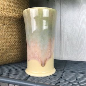 May include: A tall, ceramic vase with a light yellow base and a green, blue, and pink glaze. The glaze has a mottled effect, creating a unique and artistic look.
