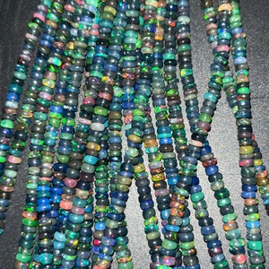 May include: A strand of black opal beads with iridescent green, blue, and purple hues. The beads are small and round, and they are strung on a clear thread.