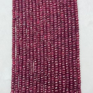 May include: A strand of deep red ruby beads, each bead is faceted and has a slightly rounded shape. The beads are strung on a clear thread and are approximately 3mm in diameter.