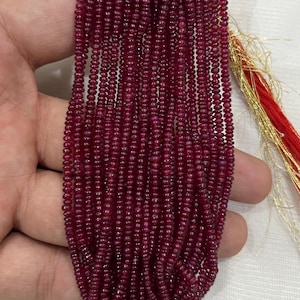 May include: A collection of small, round, deep red beads strung together. The beads are a rich, dark red colour, and appear to be polished. The strands of beads are held together. The background is a light, neutral colour.