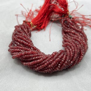 May include: A strand of small, faceted, burgundy-colored beads. The beads are tightly strung together, forming a twisted rope-like shape. A red tassel is attached at the top. The beads have a slight sparkle, suggesting they are made of a reflective material.