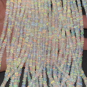 May include: A strand of white opal beads with iridescent rainbow flashes. The beads are small and round, and they are strung on a clear thread. The beads are arranged in a loose, flowing pattern.
