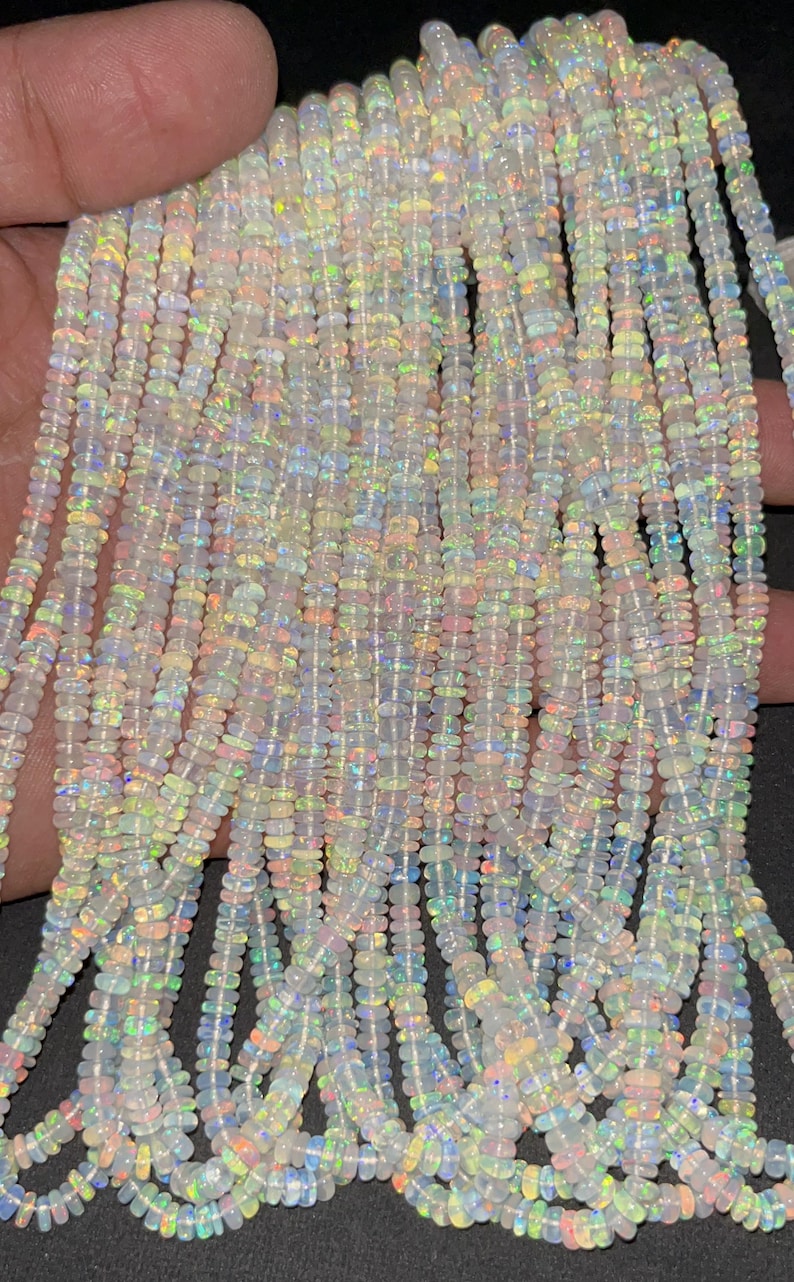 May include: A strand of white opal beads with iridescent rainbow flashes. The beads are small and round, and they are strung on a clear thread. The beads are arranged in a loose, flowing pattern.