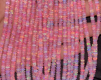 May include: Strands of pink opal beads. The beads are small, uniform in size, and have a slightly iridescent quality, with flashes of color. The beads are strung together, creating a cascading effect. The overall color palette is soft and feminine.