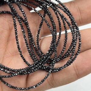 May include: A strand of black diamond beads, each bead is faceted and has a shiny, reflective surface. The beads are strung on a thin thread and are approximately 2 mm in diameter.