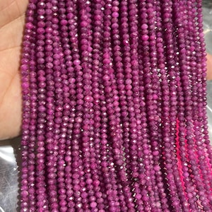 Pode incluir: Múltiplos fios de pequenas contas redondas facetadas de cor magenta profundo, enfiadas num fio cor-de-rosa brilhante. As contas têm uma superfície texturada e refletora, dispostas em linhas verticais paralelas, criando um padrão denso e uniforme.