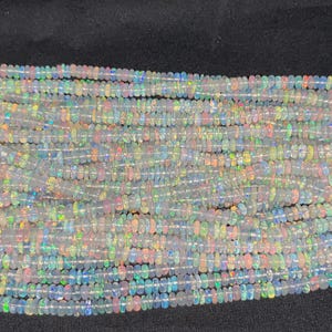May include: A strand of white opal beads with iridescent flashes of colour. The beads are small and round, and they are strung on a clear thread.