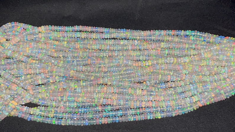 May include: A strand of white opal beads with iridescent flashes of colour. The beads are small and round, and they are strung on a clear thread.