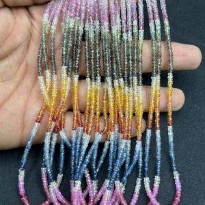 May include: A strand of colorful gemstone beads, featuring shades of pink, blue, yellow, and orange. The beads are small and round, and they are strung together on a clear thread. The strand is long and flowing, and it would make a beautiful necklace or bracelet.