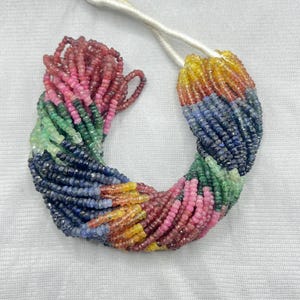 Op de afbeelding: Een kleurrijke streng edelsteen kralen in roze, groen, blauw, geel en rood. De kleine, facetgeslepen kralen zijn geregen op een wit koord. De edelstenen zijn gerangschikt in een kleurengradiënt.
