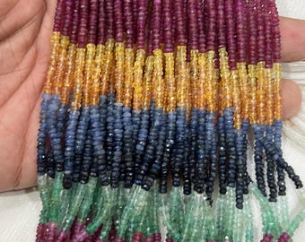 May include: Strands of colorful gemstone beads in a variety of colors, including deep red, yellow, blue, green, and black. The beads are small and faceted, and appear to be strung together. The beads are held in a hand.