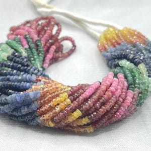 May include: A strand of colorful gemstone beads in a rainbow of hues, including pink, green, blue, and yellow. The beads are small and round, strung together on a white cord. Ideal for jewelry making.