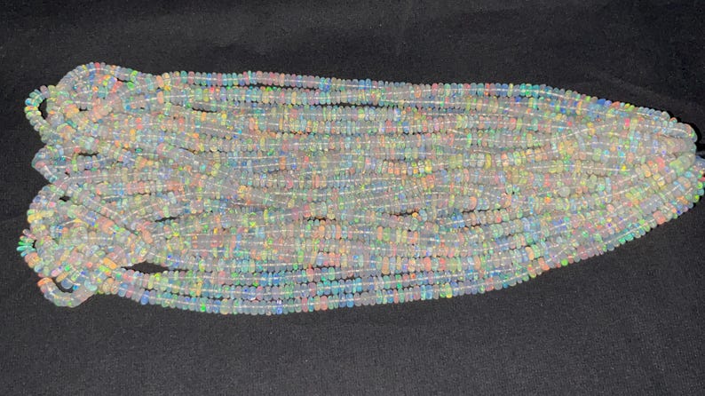 May include: A strand of white opal beads with iridescent rainbow flashes. The beads are small and round, and they are strung together on a clear thread.